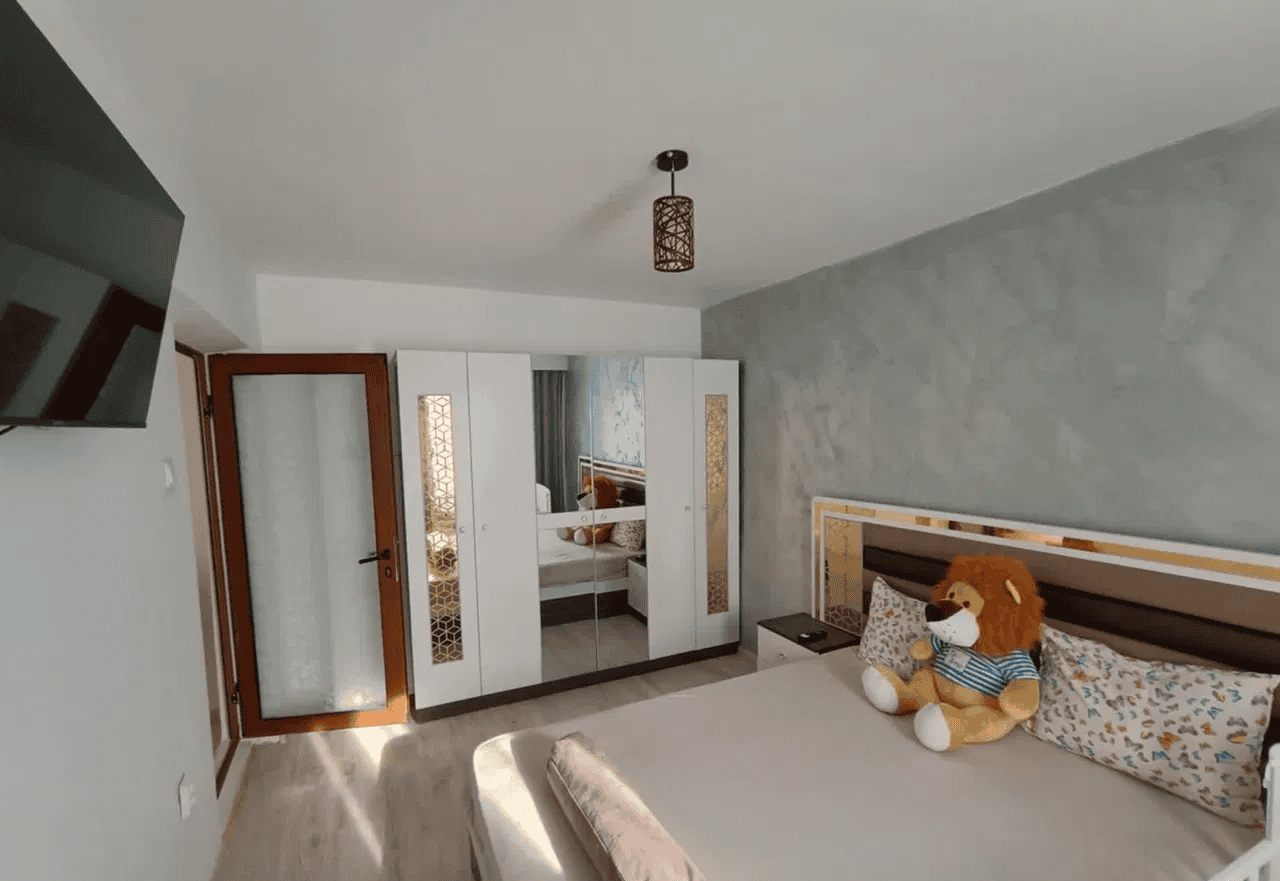 Camera de dormit cu mobilier alb, decor relaxant și jucărie de pluș pe pat.