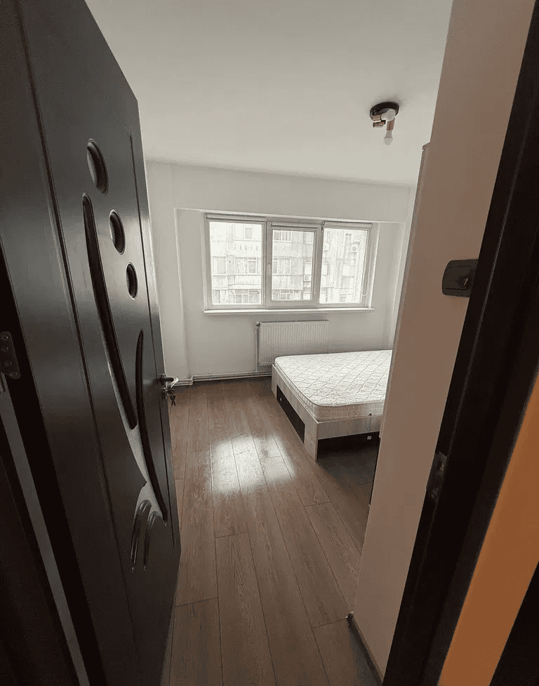 Camera de dormit spațioasă cu fereastră mare și parchet din lemn natural.