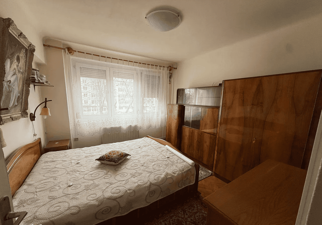 Camera de dormit cu mobilier clasic și fereastră mare pentru lumină naturală.