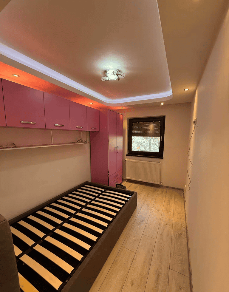 Camera de dormit modernă cu mobilier roz, pat fără saltea și lumină ambientală caldă, ideală pentru.