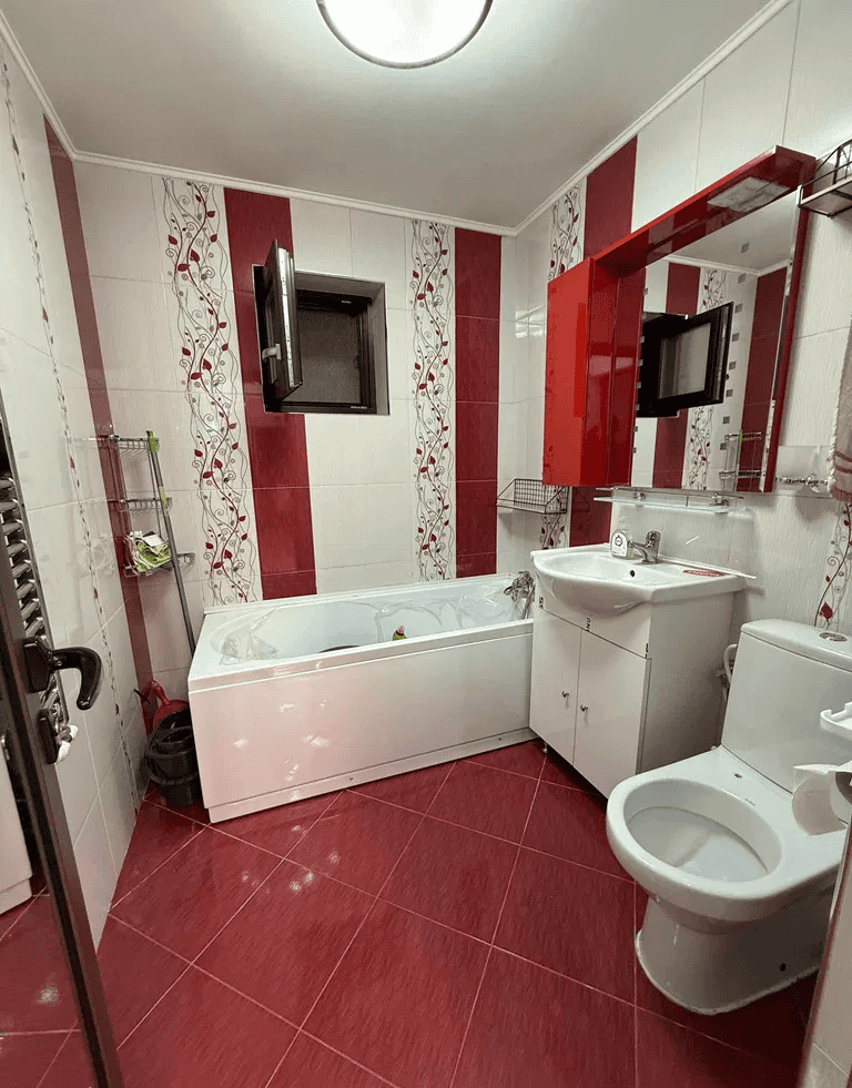 Baie modernă cu cadă, mobilier alb și oglindă mare, ideală pentru confort și funcționalitate.