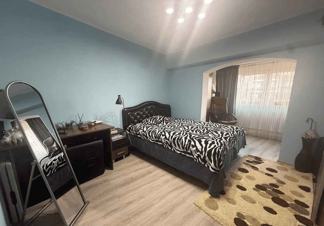 Dormitor modern cu pat și mobilier elegant, lumină naturală și decor confortabil.