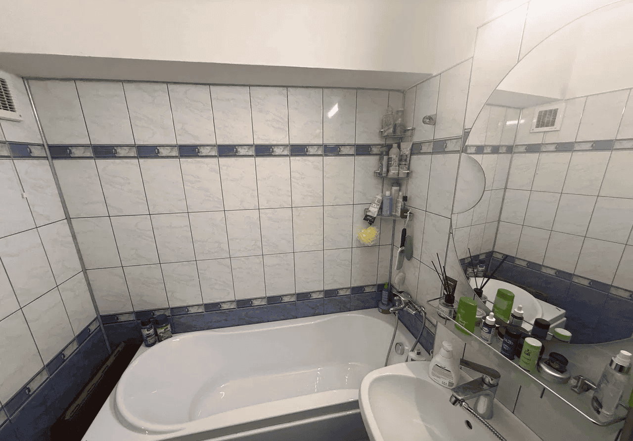 Baie mică cu cadă și oglindă, decorată cu plăci ceramice albastre și albe.