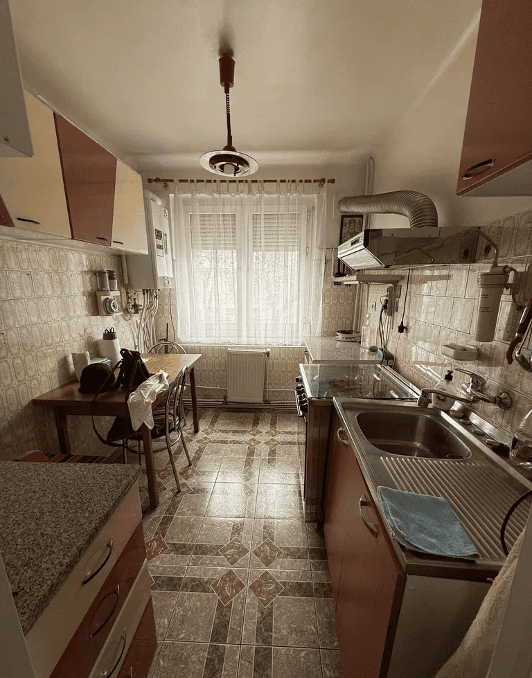 Bucătărie cu mobilier modern, chiuvetă și geam mare pentru lumină naturală.