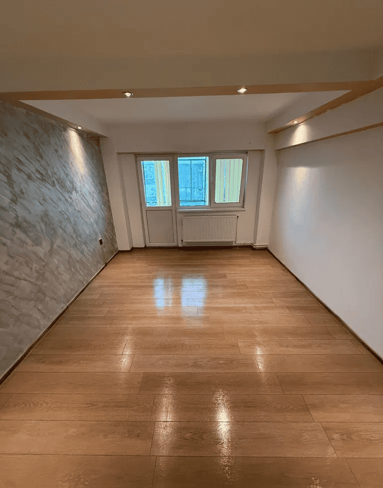 Camera de zi spațioasă cu parchet din lemn și ferestre mari pentru lumină naturală.