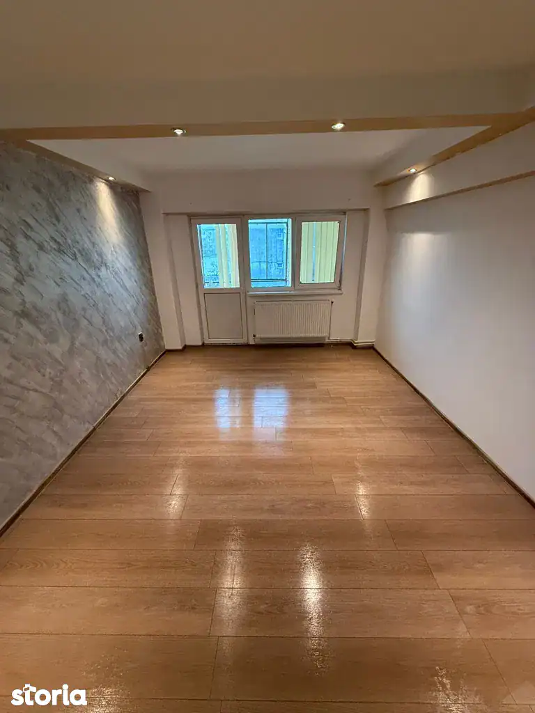 Spațiu de locuit luminos cu ferestre mari și podea de lemn.